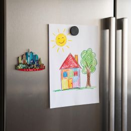 Wooden Madrid skyline magnet on a fridge next to a child’s drawing